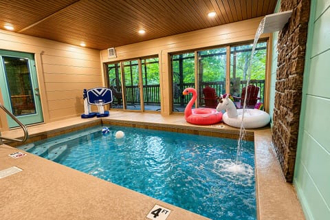 Private indoor pool with waterfall feature and wooded deck views