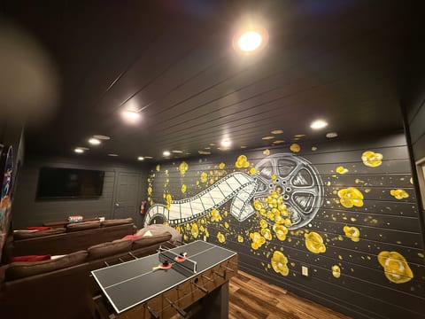 Private movie lounge with mural, comfy seating, TV, and game table