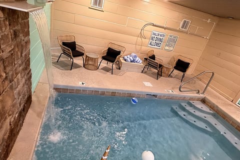 Indoor pool with waterfall feature and cozy poolside seating
