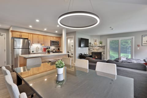 The dining table sits between the full kitchen and the fireside living area, with patio doors beyond.