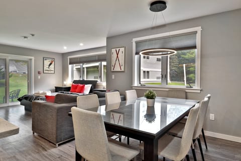 A table with six chairs sits by the sofa, wide windows and patio doors.