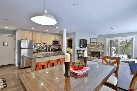 The dining table, four-seat island, gas fireplace and patio doors share one open room.