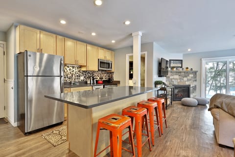 The full kitchen has four island stools, stainless appliances and the gas fireplace just beyond.