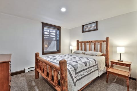 A queen bed sits between two lamps, with windows on adjacent walls bringing daylight into the room.