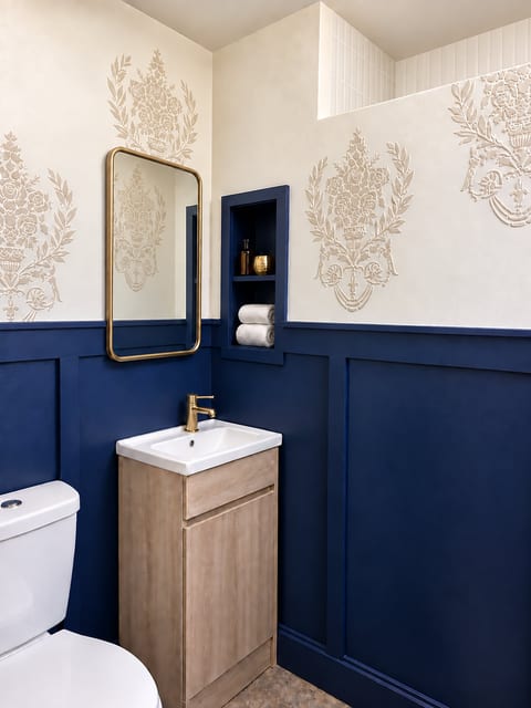 Elegant powder room with navy paneling, brass accents, and designer wallpaper