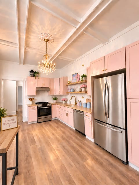 Chic pink kitchen with chandelier, stainless appliances, and lofty ceilings