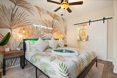 Primary king suite — palm-leaf mural, neon accent, woven pendant lights, and barn door entry to private spa ensuite. St. Petersburg, FL vacation rental.