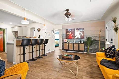 Open-plan living and kitchen — 65-inch smart TV, breakfast bar with 4 stools, and mustard yellow sofas. 4-bedroom vacation rental, St. Petersburg, FL.
