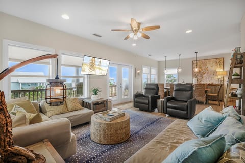 Spread out after a beach day — someone on the sectional, someone at the table, the deck doors open to the breeze. One big open room, so nobody misses the story.