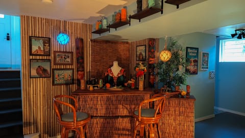 The Tiki Lounge — a playful mid-century inspired lower level with a bamboo-wrapped tiki bar, tropical lighting, and vintage island-inspired details throughout.