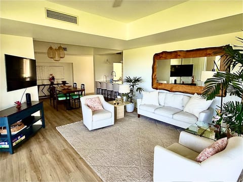 Bright, open-concept living space featuring comfortable seating, a Smart TV, dining area, breakfast bar, tropical décor, and a fully equipped kitchen—perfect for relaxing after a day exploring Hawaii.