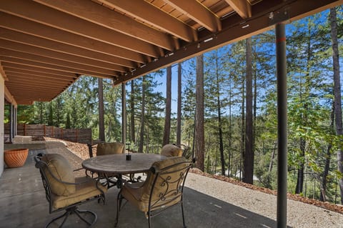 Covered outdoor patio with seating and dining for four, string lights, and peaceful views of the surrounding pines.