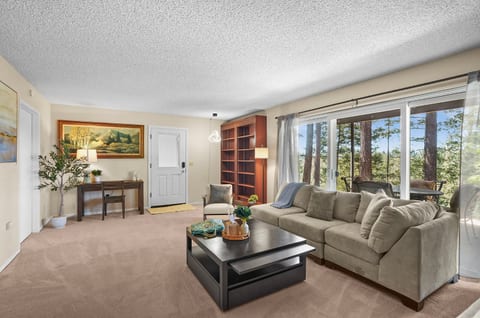 Spacious and inviting living room with comfortable seating, a Smart TV, and large windows that bring in plenty of natural light and views of the surrounding pines.