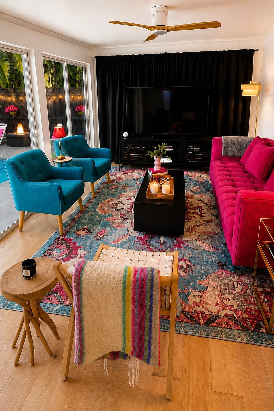 The living room at Pink Posh Inn doesn’t do subtle — fuchsia velvet sofa, teal accent chairs, a vibrant medallion rug, and floor-to-ceiling black drapes for the ultimate movie night. Step outside and the pool is waiting.