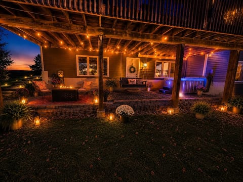 A fully lit private patio, cozy seating, and a glowing hot tub, firepit and propane grill.