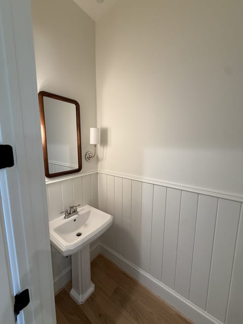 Charming half bath with pedestal sink, wainscoting, and warm wood floors