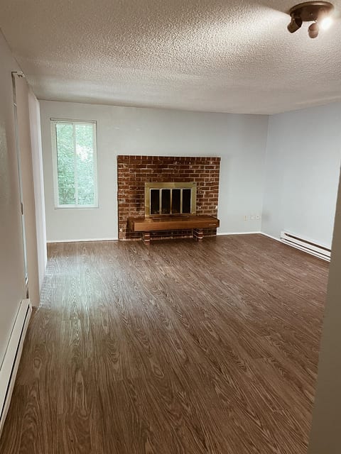Bright, spacious living room with warm floors and cozy brick fireplace