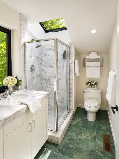 Bright full bathroom featuring a marble-lined glass-enclosed shower, marble vanity, and skylight that fills the space with natural light. Fresh towels and a clean, comfortable layout make it easy to refresh and unwind.