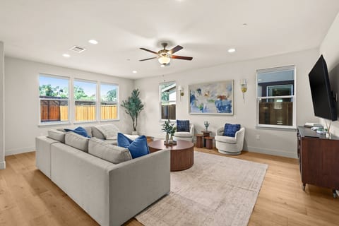 A spacious, light-filled living room with comfortable seating, warm wood floors, and a Smart TV. Large windows bring in plenty of natural light, and the open layout creates an inviting space to relax and gather.