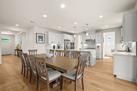 A spacious open-concept kitchen and dining area designed for gathering. The fully stocked kitchen features a large island, modern appliances, generous counter space, and plenty of cabinetry. The dining table comfortably seats up to 10 guests.