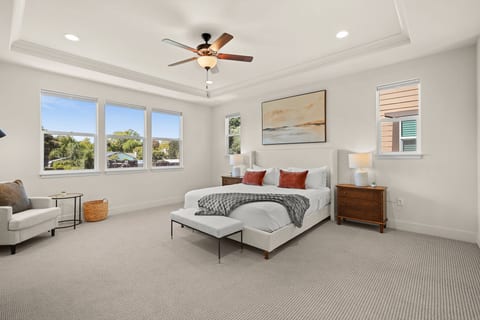 A spacious primary suite with a king bed, comfortable sitting area, elegant furnishings, and abundant natural light. The tray ceiling and generous layout create an open and relaxing retreat with plenty of room to unwind.
