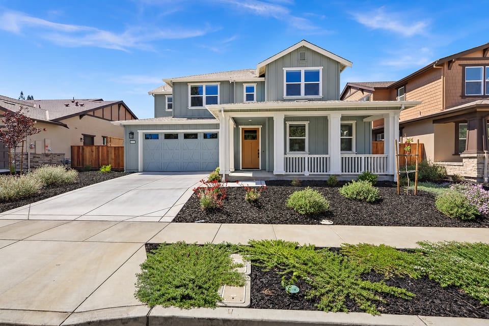 A welcoming exterior view of this newly built Napa home with a covered front porch, attractive landscaping, and an attached two-car garage. The bright, beautifully maintained entrance creates a warm welcome.