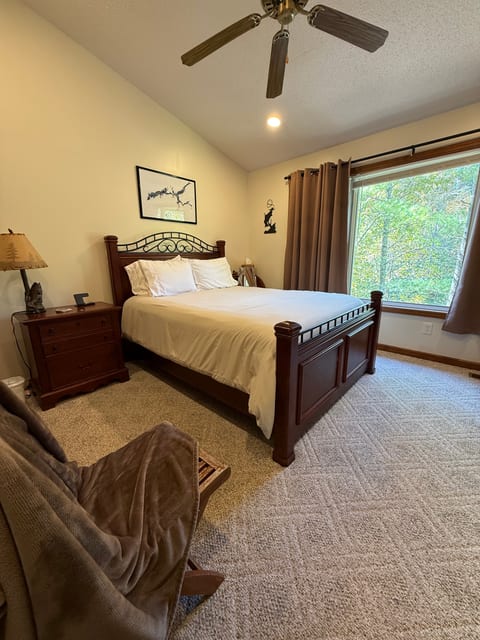 Your peaceful retreat at the end of the day—a comfortable queen bed, cozy seating, blackout curtains, ceiling fan, and a beautiful wooded lake view from the large window.