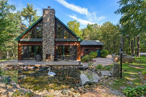Rustic log cabin with soaring windows, stone fireplace, and serene pond