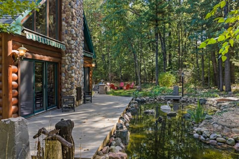 Rustic woodland cabin with stone chimney, deck, and peaceful pond views