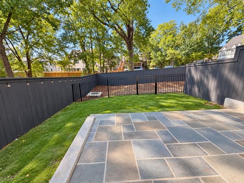 Private fenced yard with stone patio, lawn, and shaded outdoor space