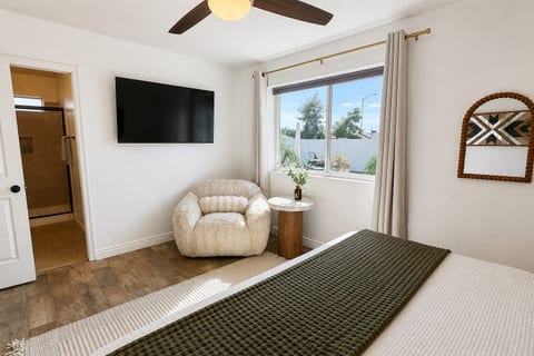 Bright bedroom with natural light, TV, cozy chair, and ensuite bath
