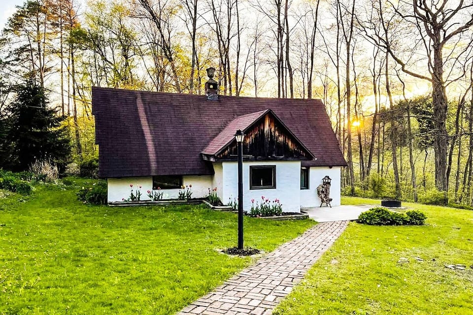 Escape to our charming country side cottage nestled in a verdant forest. Admire the cozy scenery, homely white facade, and a winding brick path leading to sunlit expanses. A tranquil retreat for nature lovers! You can see the lake through the trees!
