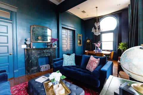 Experience tranquility in our living room with serene blue walls, a plush velvet couch and large coffee table. A mirror above the couch adds a spacious feel.