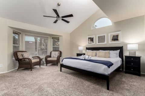 Unwind in a luxurious king bed beneath vaulted ceilings with wicker lounge chairs, stylish nightstands, and plush carpet for ultimate relaxation.