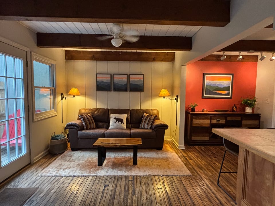 Cozy rustic living room with leather sofa, warm beams, and outdoor access