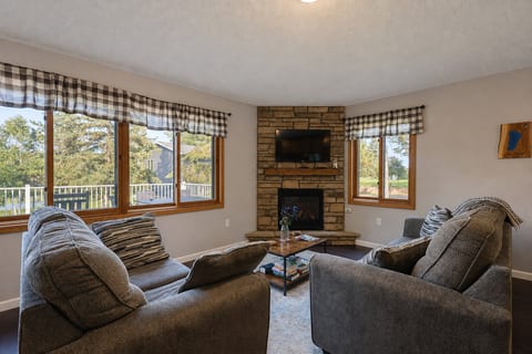 Cozy living room with stone fireplace, TV, and bright scenic windows