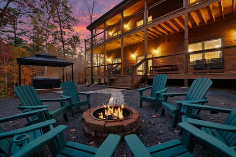 Adirondack chairs circle the fire pit as the Smoky Mountain sky turns pink behind the cabin. Wraparound deck and covered hot tub just steps away — room for the whole group to spread out, inside and out.