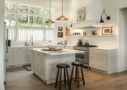 “Chef-inspired kitchen featuring a professional range, large sink, beverage fridge, and spacious island perfect for gathering. Vaulted ceilings, a large window, and abundant natural light create a bright and inviting space.