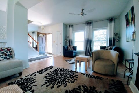 View of 2/3 of the living room from the middle seating area near the fireplace. Front door and stairs to the second level also. Lots of light and windows in an open floor plan.