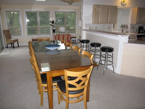 View of the dining table which has 10 chairs and extra seating can be accommodated using the benches in the sunroom. Three bar stools on the right face the kitchen. Open floor plan.