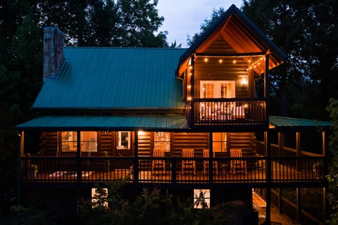 Cozy log cabin with wraparound deck and glowing balcony at dusk