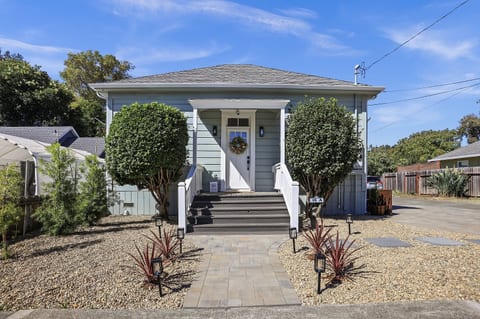 A charming front view of this light blue Napa cottage with a welcoming covered porch, mature landscaping, and a paver walkway leading to the front door.