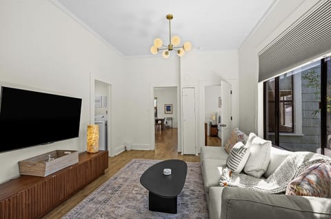 The living room features a large Smart TV, cozy seating, and an open layout that flows toward the bedrooms and kitchen.