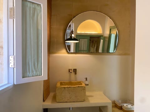 Boutique-style bath with stone sink, arched mirror, and warm lighting