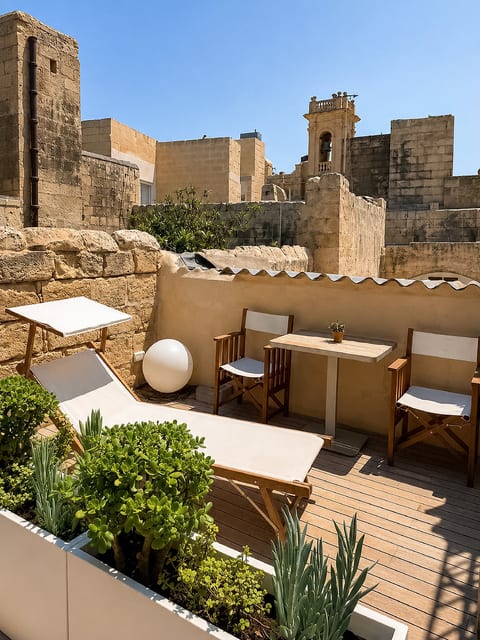 Sunny rooftop terrace with loungers, dining nook, and historic stone views