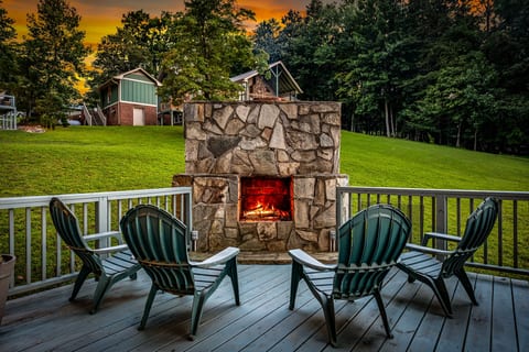 Cozy deck with stone fireplace, sunset views, and peaceful wooded lawn