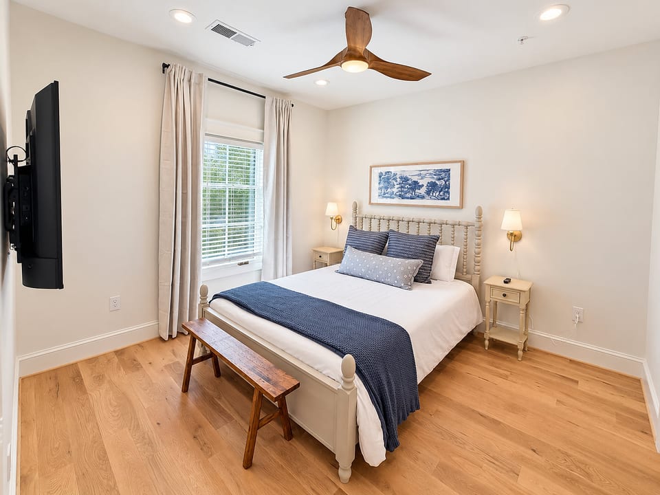 Bright, cozy bedroom with TV, ceiling fan, and elegant blue accents
