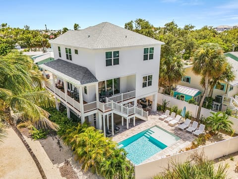 Aerial view of The Shell House featuring the private heated pool, oversized sun shelf, tropical landscaping, and spacious covered porches.