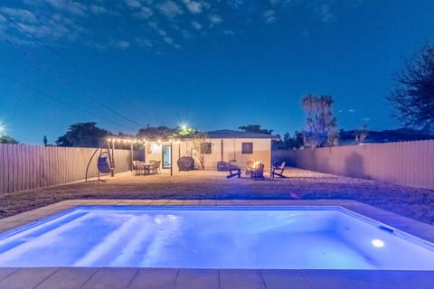 Private backyard oasis with lit pool, fire pit, and patio seating