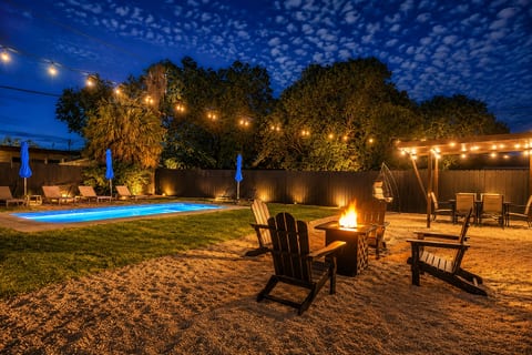 Resort-style backyard with pool, fire pit, and twinkling evening lights